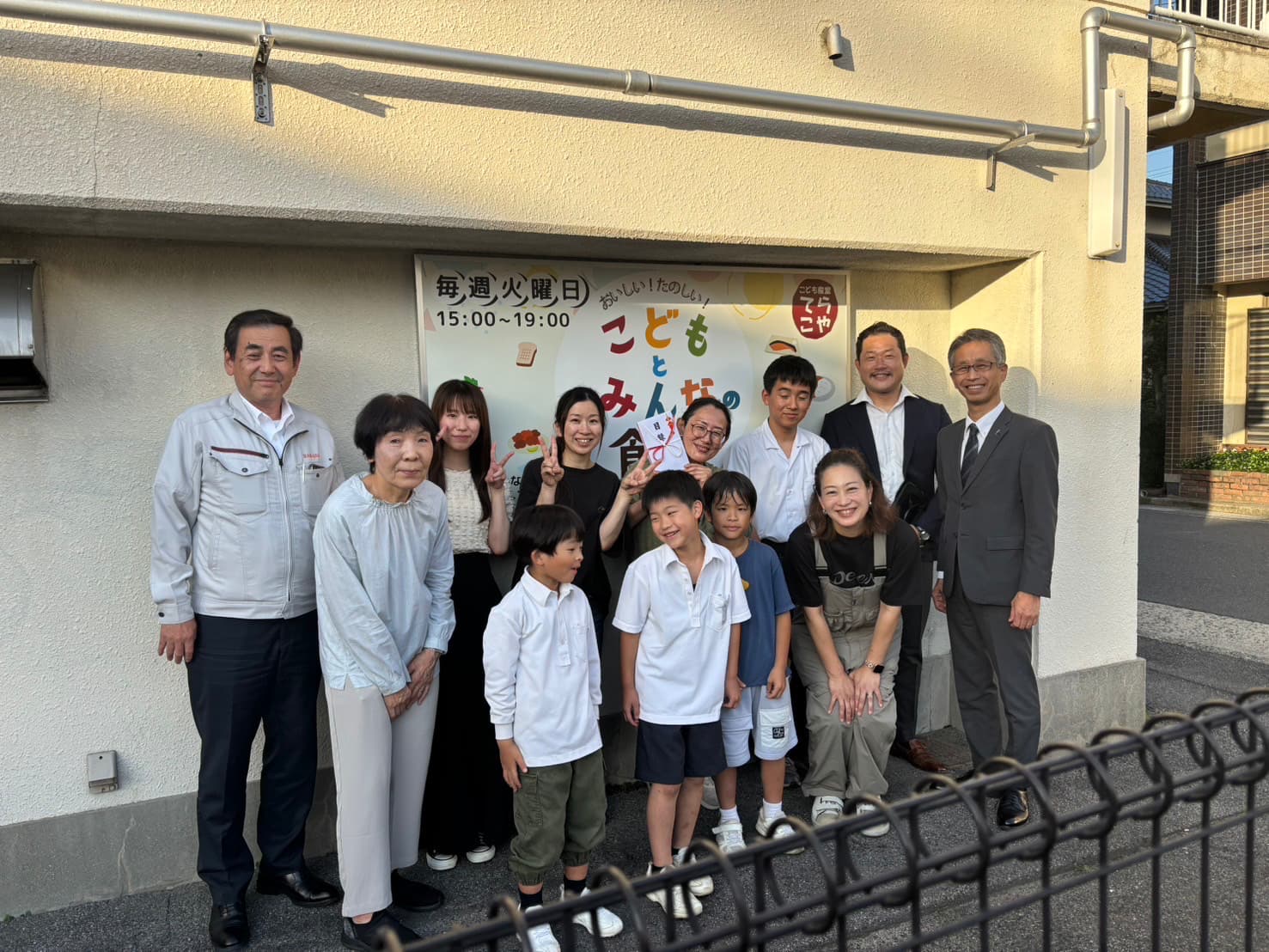 贈呈品の看板の前で、子どもたち、関係者の皆さまと | 地域まちづくり貢献型私募債の発行と贈呈式の実施について | お知らせ | 株式会社原田組